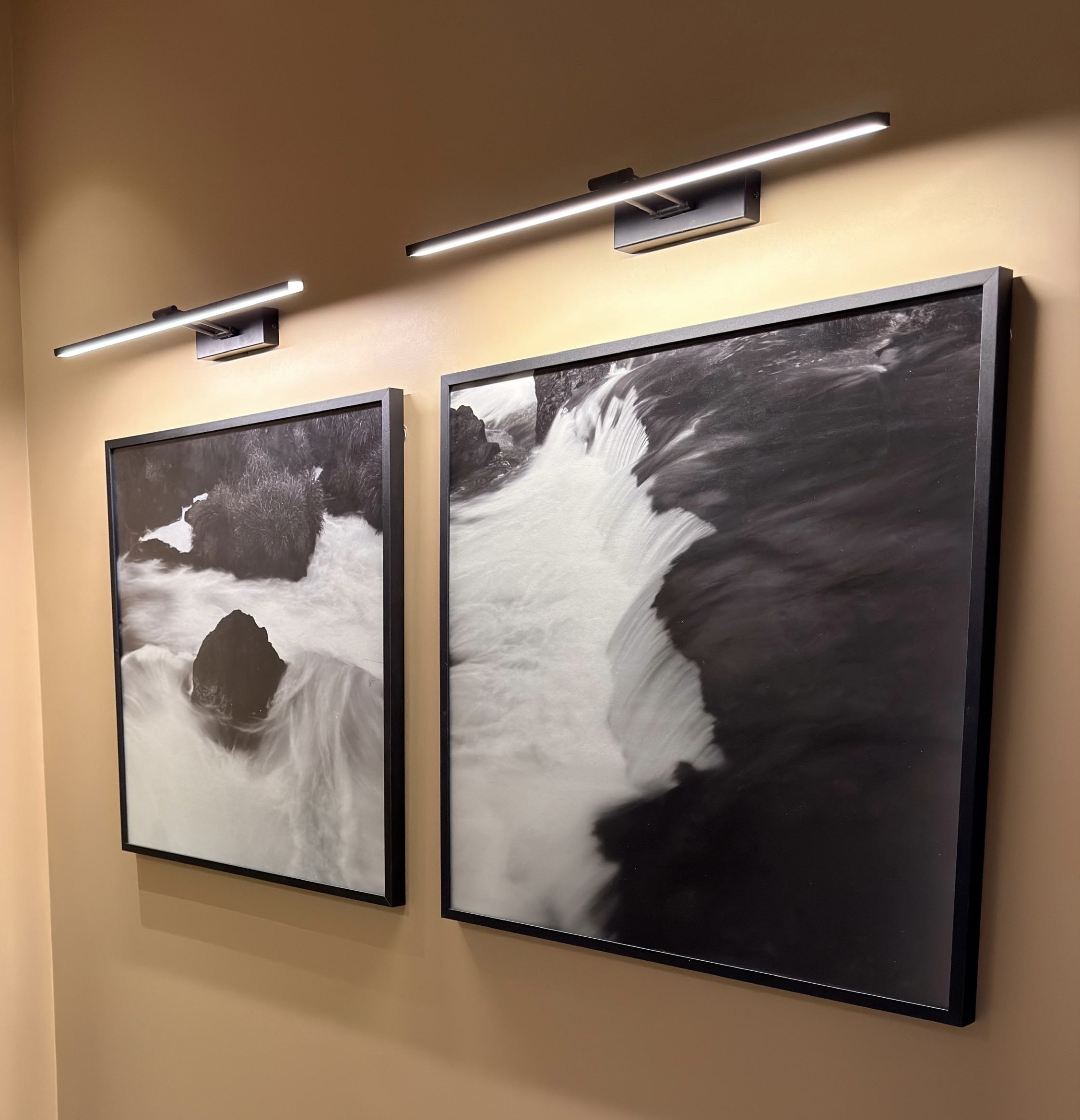 Two framed black-and-white photographs of water and rocks, illuminated by wall-mounted picture lights